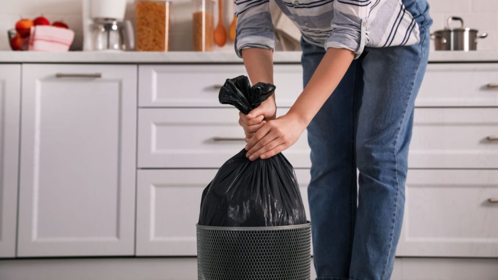 Decluttering home by throwing unused items in trash bag