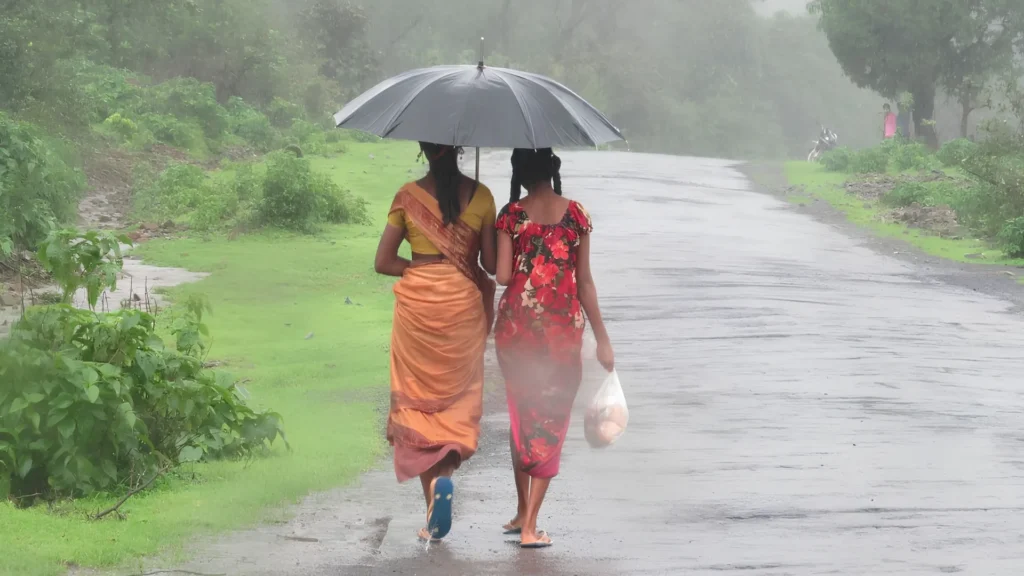 Mother and daughter walking with umbrella during monsoon